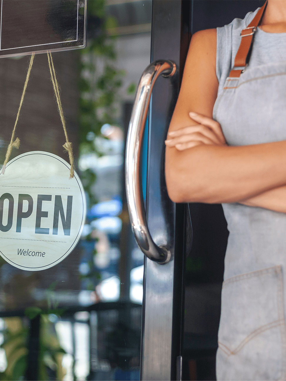 Woman business owner in apron standing by building door with an "open" sign hanging from the window.